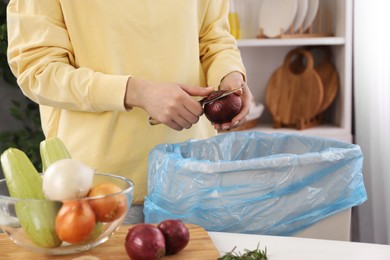 Photo of Woman peeling fresh onion above garbage bin indoors, closeup