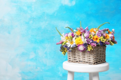 Wicker basket with beautiful wild flowers on table against color background