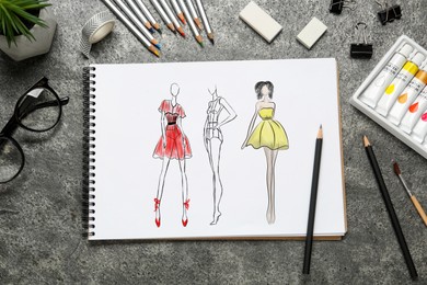 Image of Sketches of different clothes in pad on grey textured table. Fashion designer's desk with stationery, flat lay