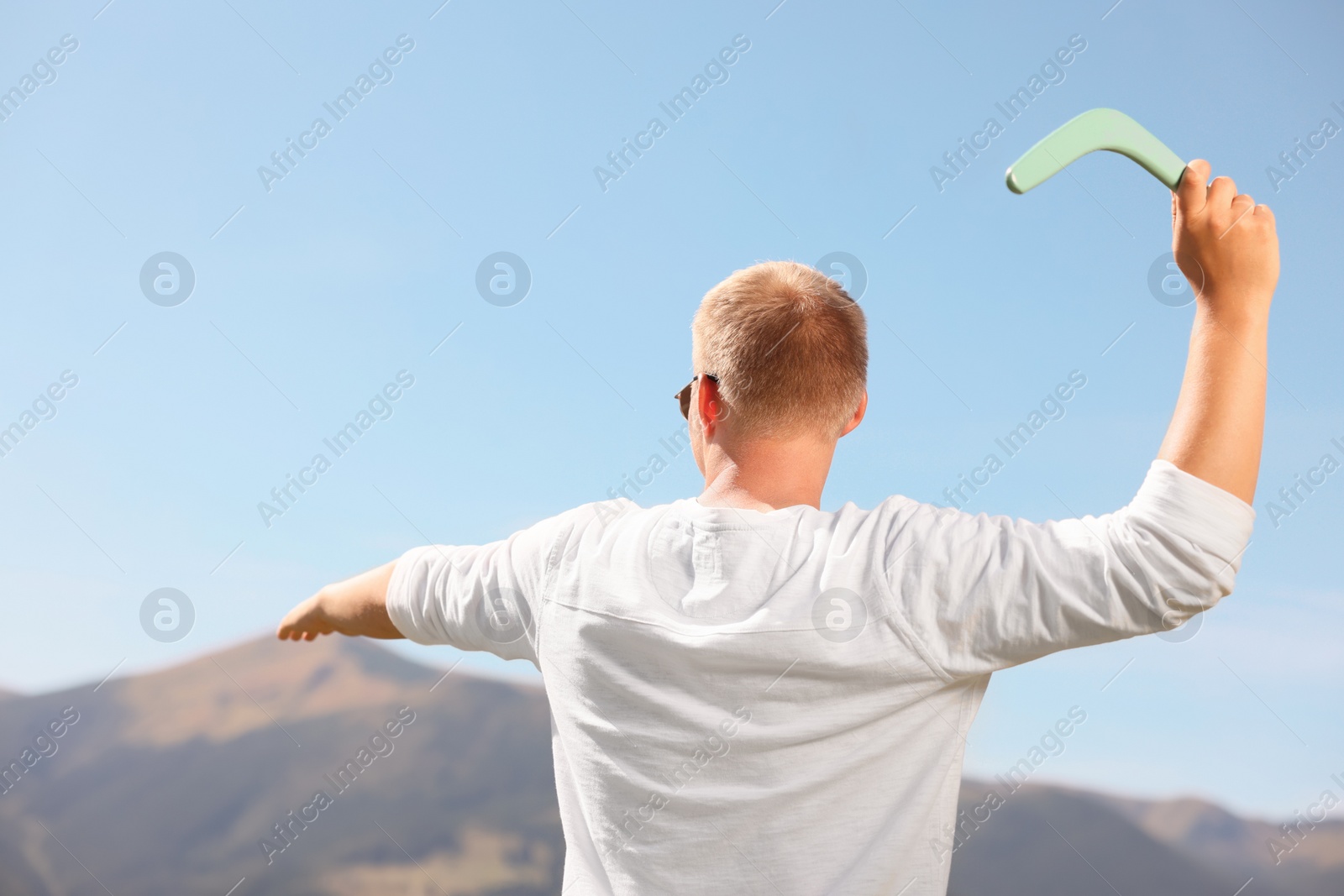 Photo of Man throwing boomerang in mountains on sunny day, back view