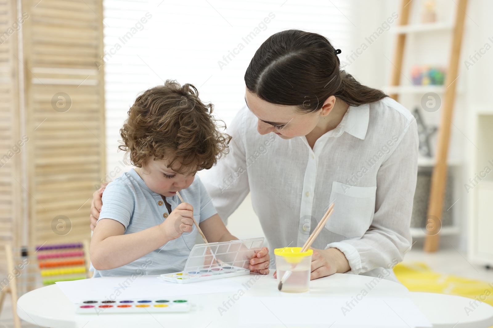 Photo of Mother and her little son painting with watercolor at home