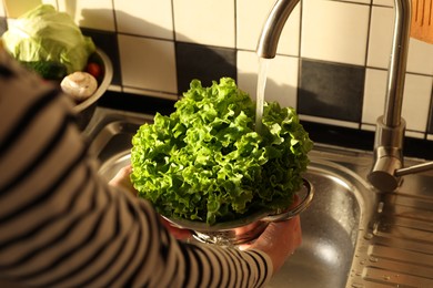 Woman washing fresh lettuce leaves in metal colander, closeup