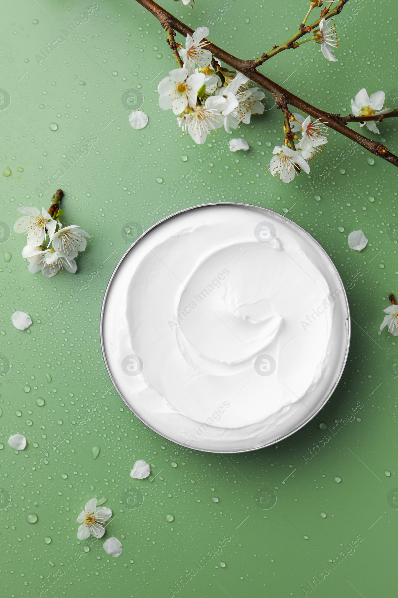 Photo of Flat lay composition with jar of face cream and flowers on wet green surface