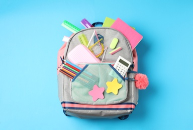 Photo of Stylish backpack with different school stationery on light blue background, top view. Back to school