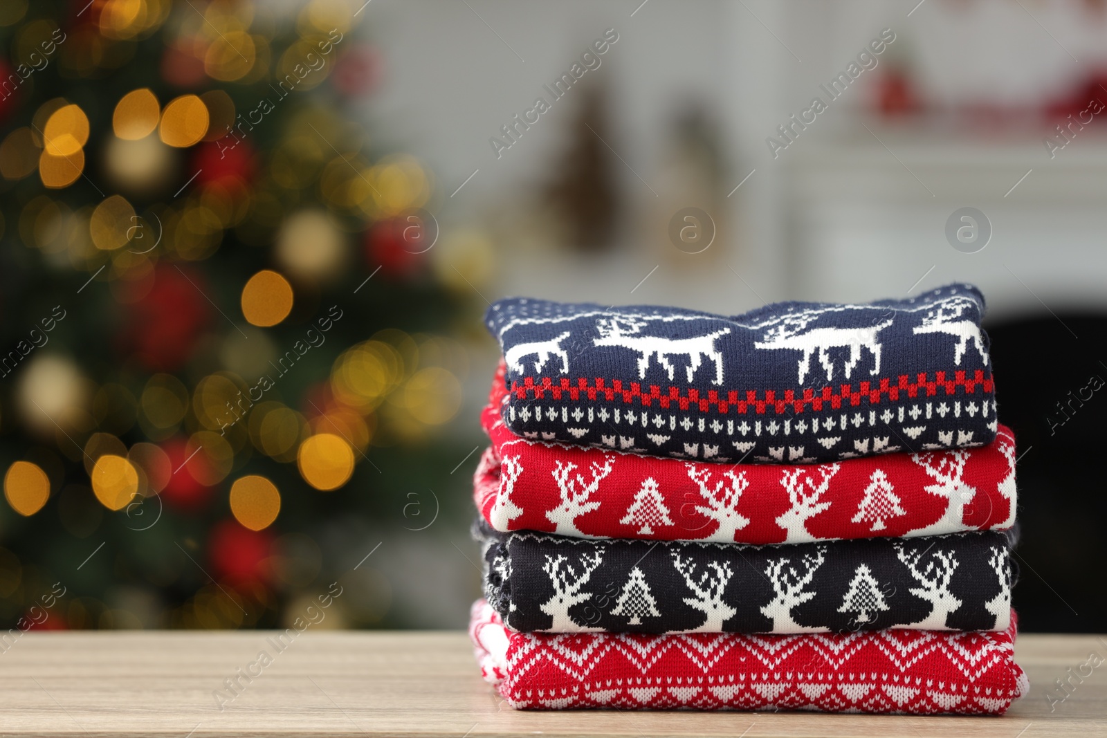 Photo of Stack of different Christmas sweaters on table against blurred lights, space for text