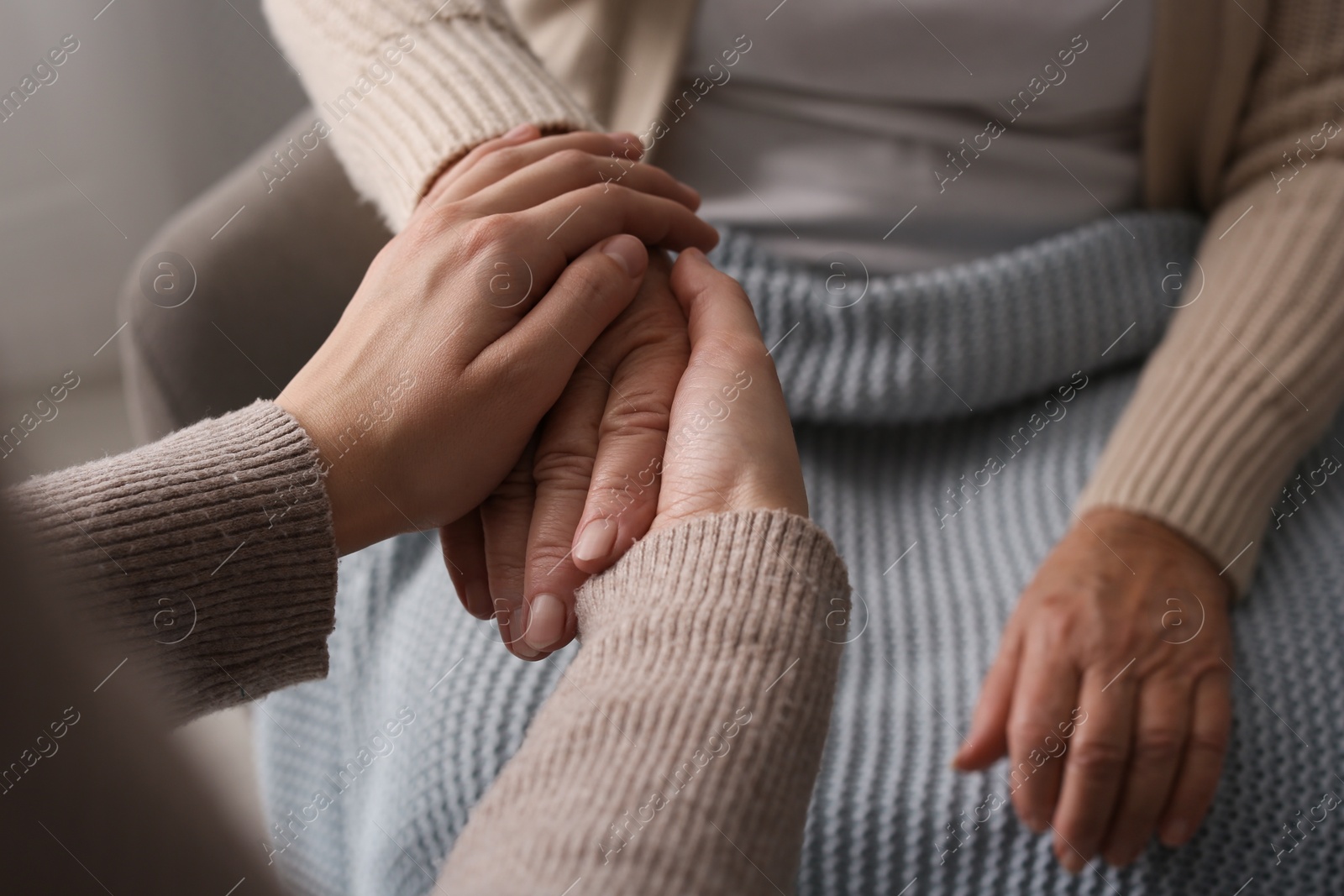 Photo of Young and elderly women holding hands together indoors, closeup