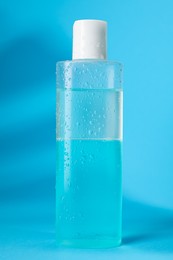 Photo of Wet bottle of micellar water on light blue background