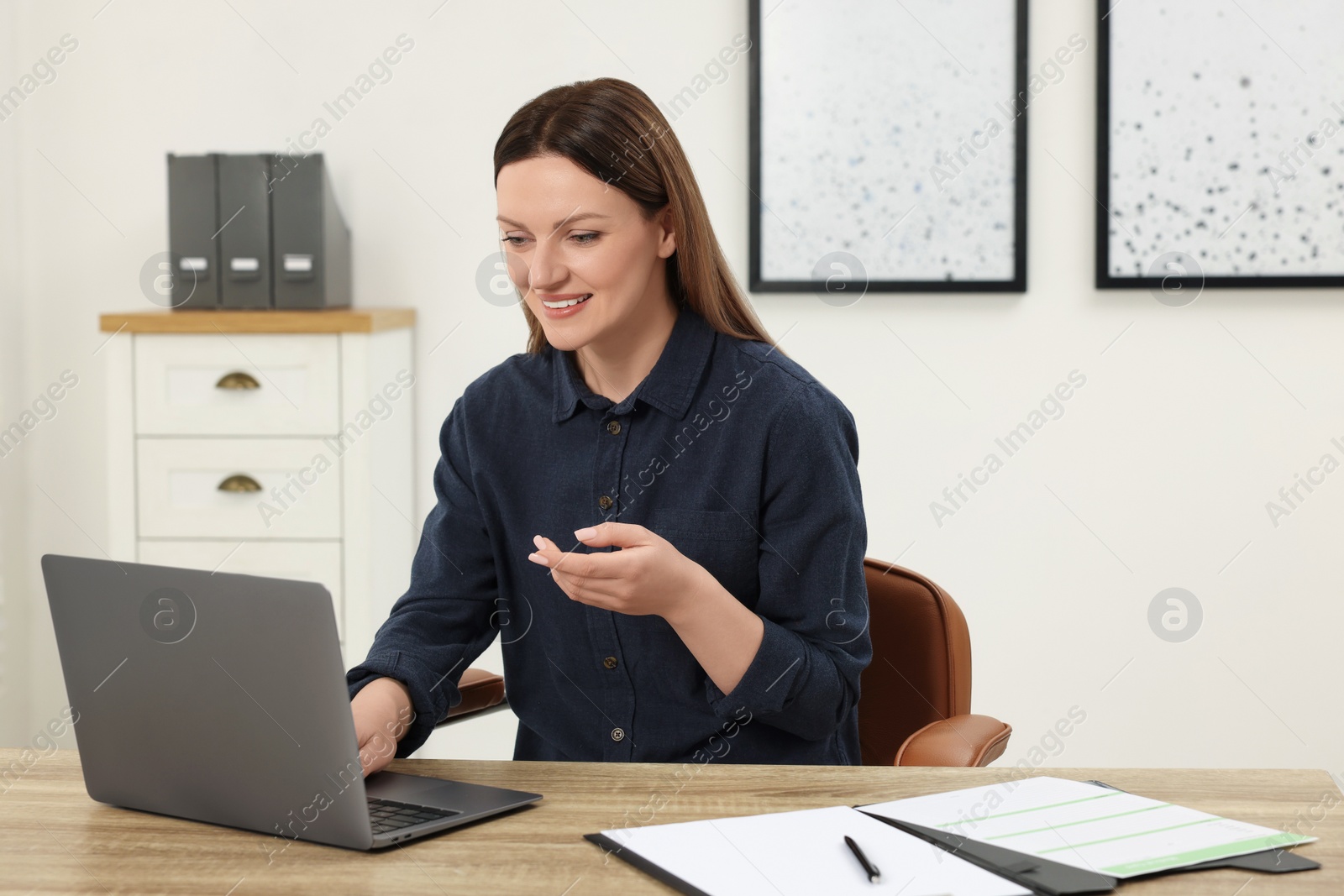 Photo of Woman having video chat via laptop at wooden table in office