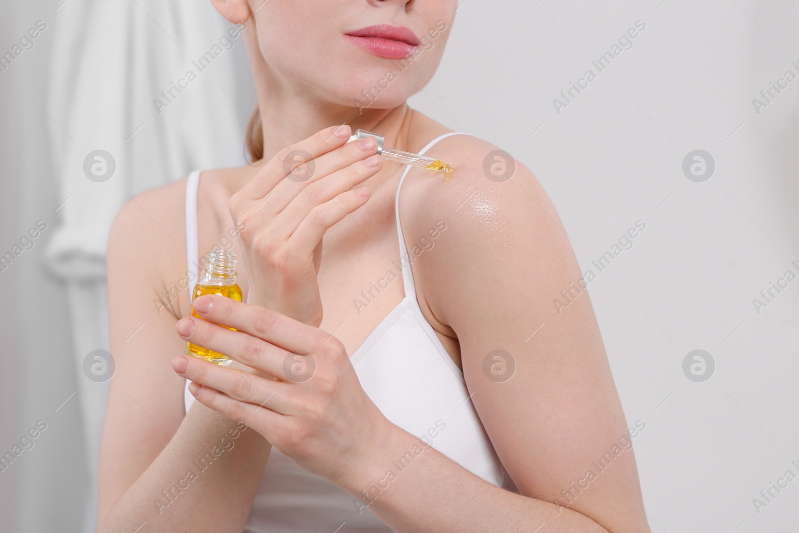 Photo of Woman applying essential oil onto shoulder in bathroom, closeup