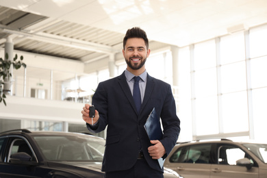 Salesman with key and clipboard in car salon