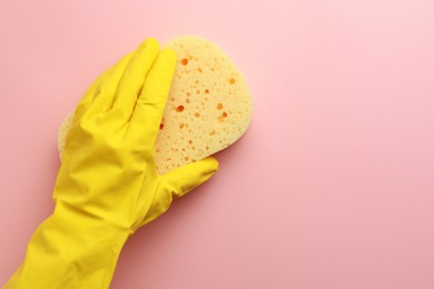 Cleaner in rubber glove holding new yellow sponge on pink background, top view. Space for text