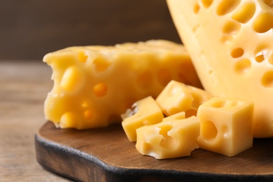 Photo of Pieces of delicious cheese and board on wooden table, closeup