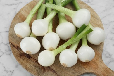 Photo of Wooden board with green spring onions on white marble table, closeup