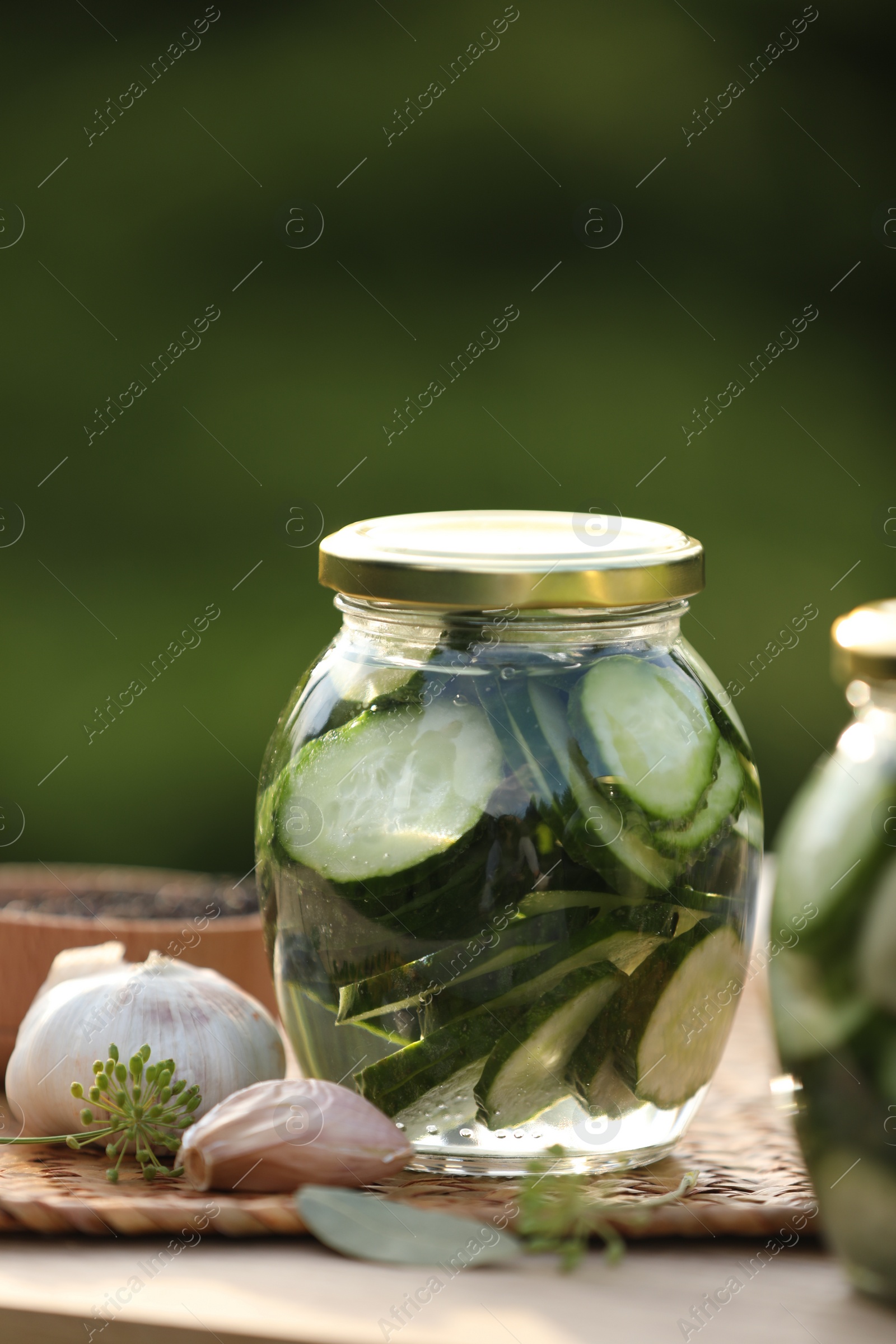 Photo of Jar of delicious pickled cucumbers and ingredients on wooden table against blurred background