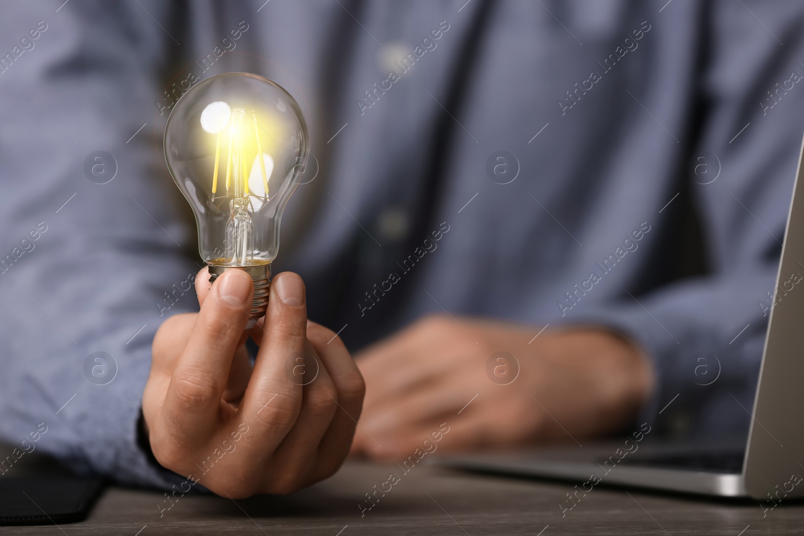 Photo of Glow up your ideas. Closeup view of man holding light bulb while working at wooden desk, space for text