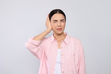 Young woman suffering from ear pain on light grey background