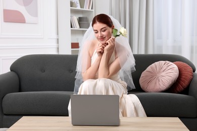 Photo of Beautiful bride with rose using laptop in living room