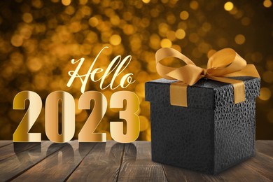 Image of Hello 2023. Beautiful gift box on wooden table against blurred festive lights, bokeh effect