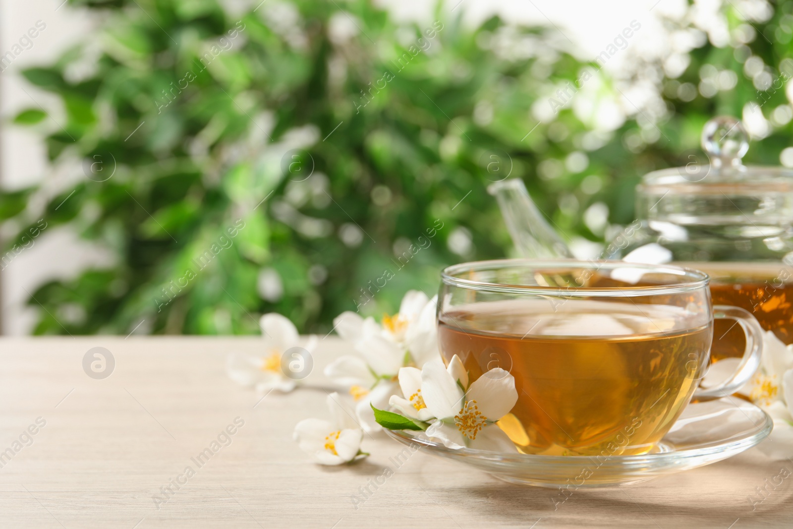Photo of Aromatic jasmine tea and fresh flowers on wooden table, space for text