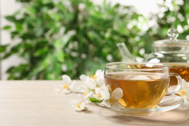 Photo of Aromatic jasmine tea and fresh flowers on wooden table, space for text