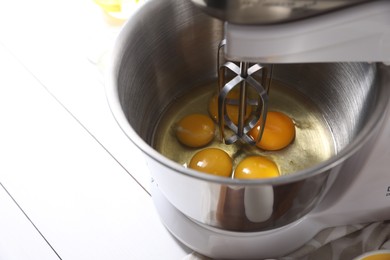 Photo of Making dough. Raw eggs in bowl of stand mixer on white table, closeup