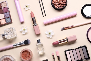 Flat lay composition with different makeup products and beautiful spring flowers on beige background