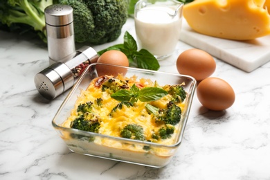 Photo of Tasty broccoli casserole in baking dish on white marble table