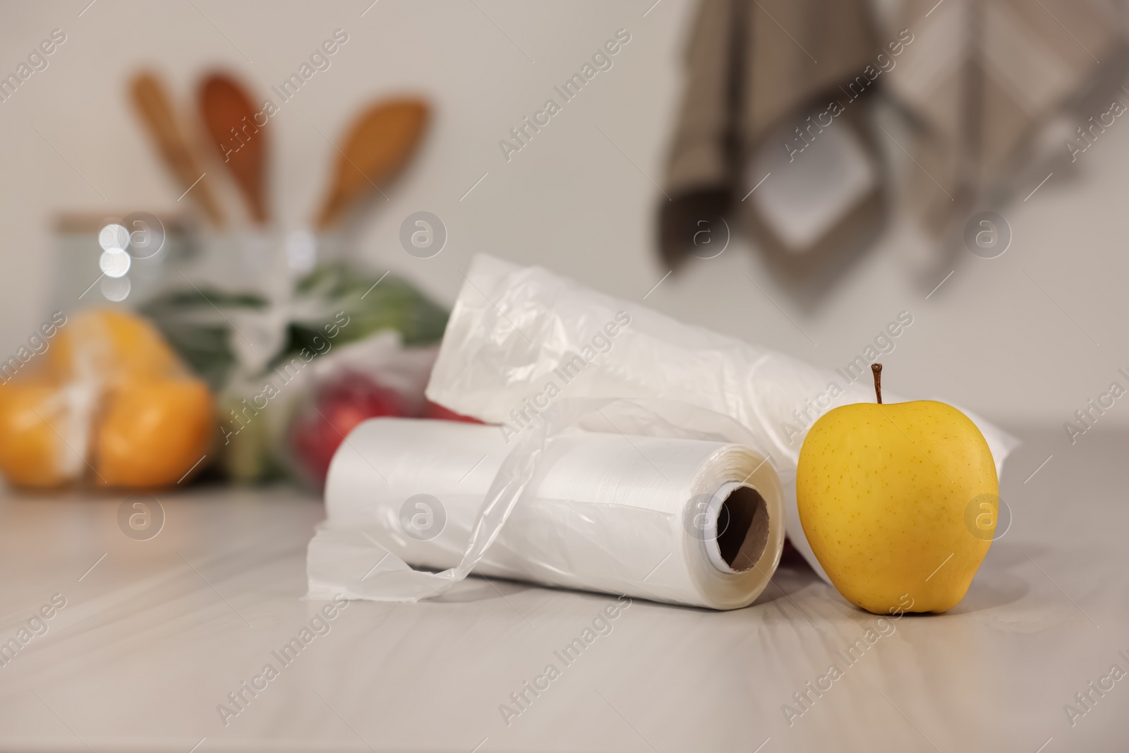Photo of Rolls of plastic bags and fresh apple on white table