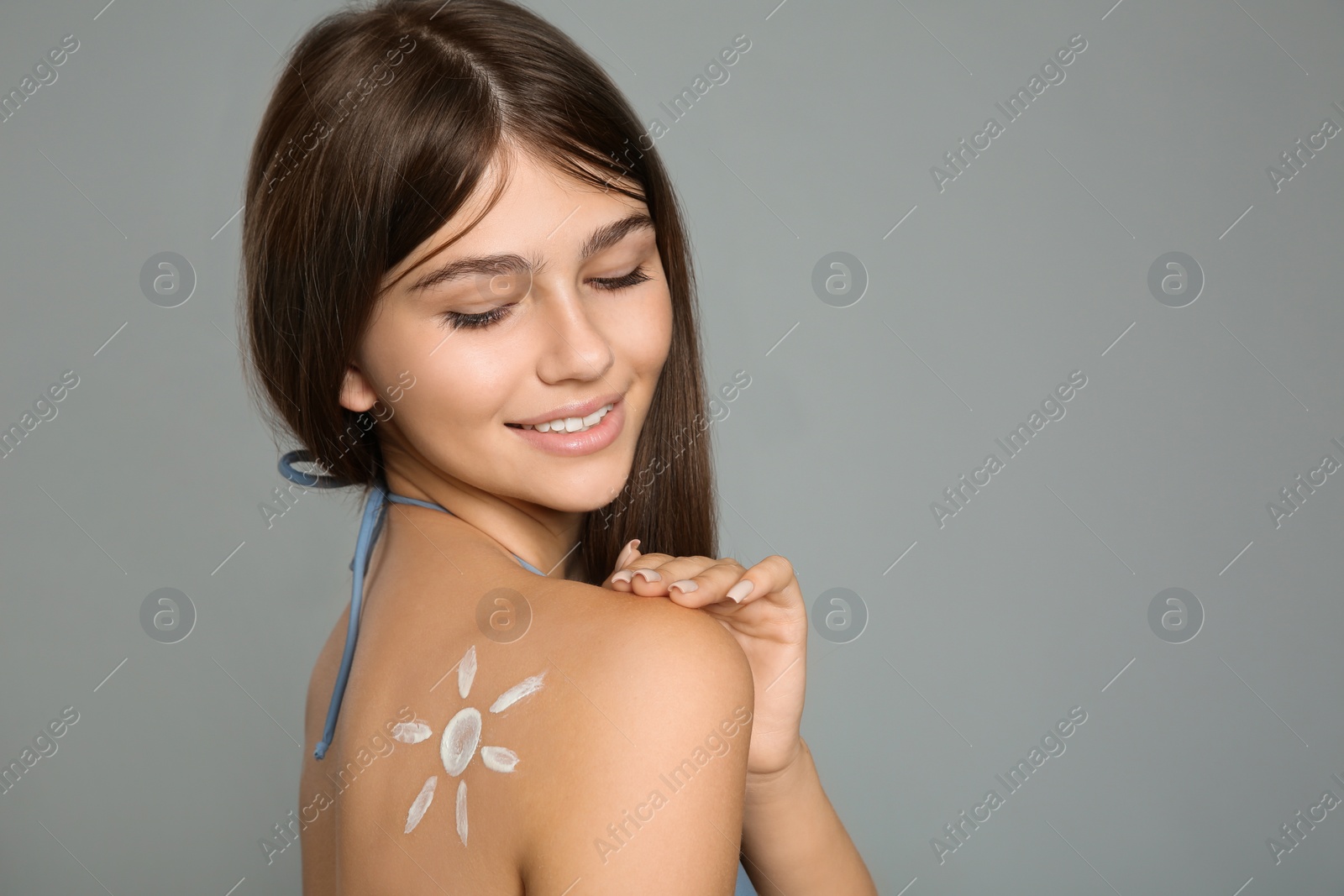 Photo of Teenage girl with sun protection cream on her back against grey background. Space for text