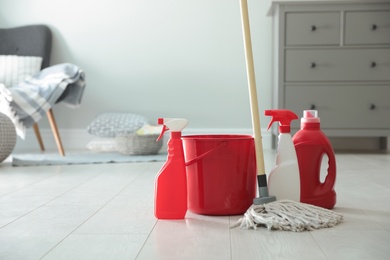 Photo of Bucket, mop and different cleaning products on floor indoors. Space for text