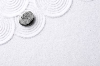 Photo of Zen garden stones on white sand with pattern, top view. Space for text