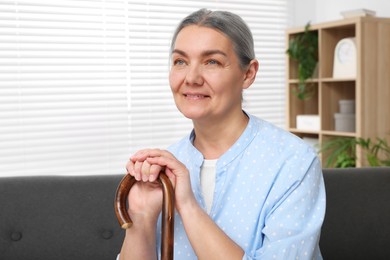 Photo of Senior woman with walking cane sitting on sofa at home. Space for text