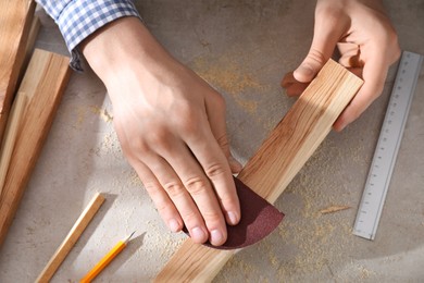 Photo of Man polishing wooden plank with sandpaper at grey table, top view