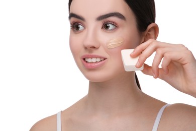 Teenage girl applying foundation on face with makeup sponge against white background