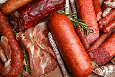 Different types of sausages with rosemary as background, flat lay