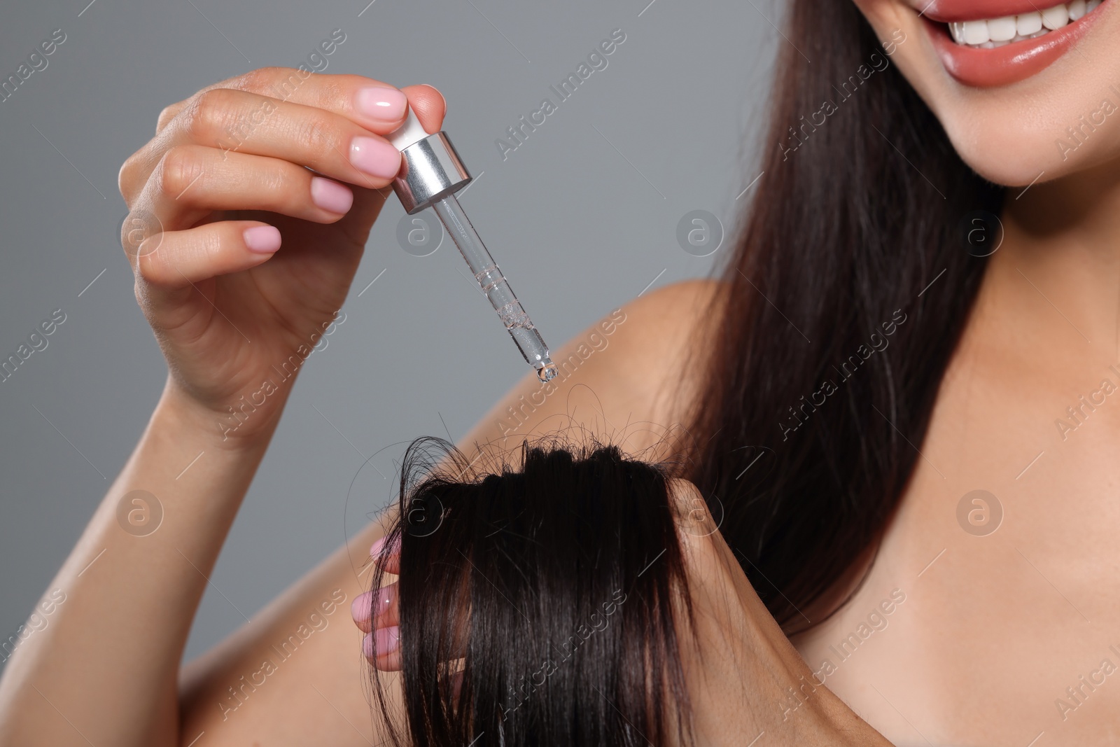 Photo of Woman applying hair serum on grey background, closeup. Cosmetic product