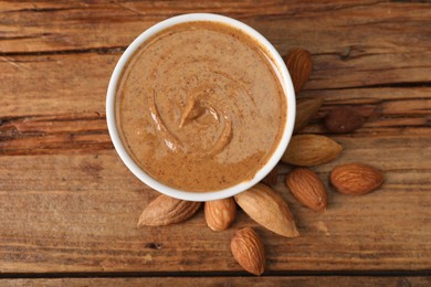 Photo of Delicious nut butter in bowl and almonds on wooden table, top view