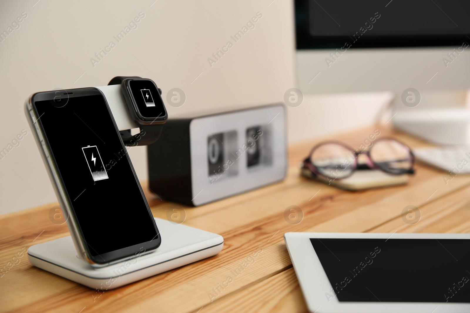 Photo of Mobile phone and smartwatch with wireless charger on wooden table. Modern workplace accessory