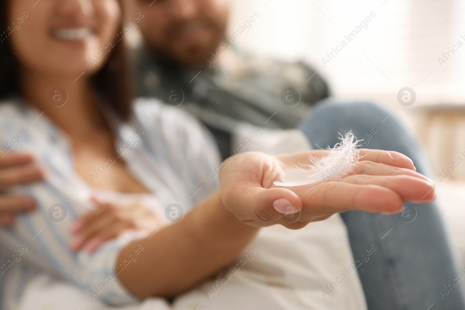 Photo of Happy couple resting after fun pillow fight at home, focus on hand with feather