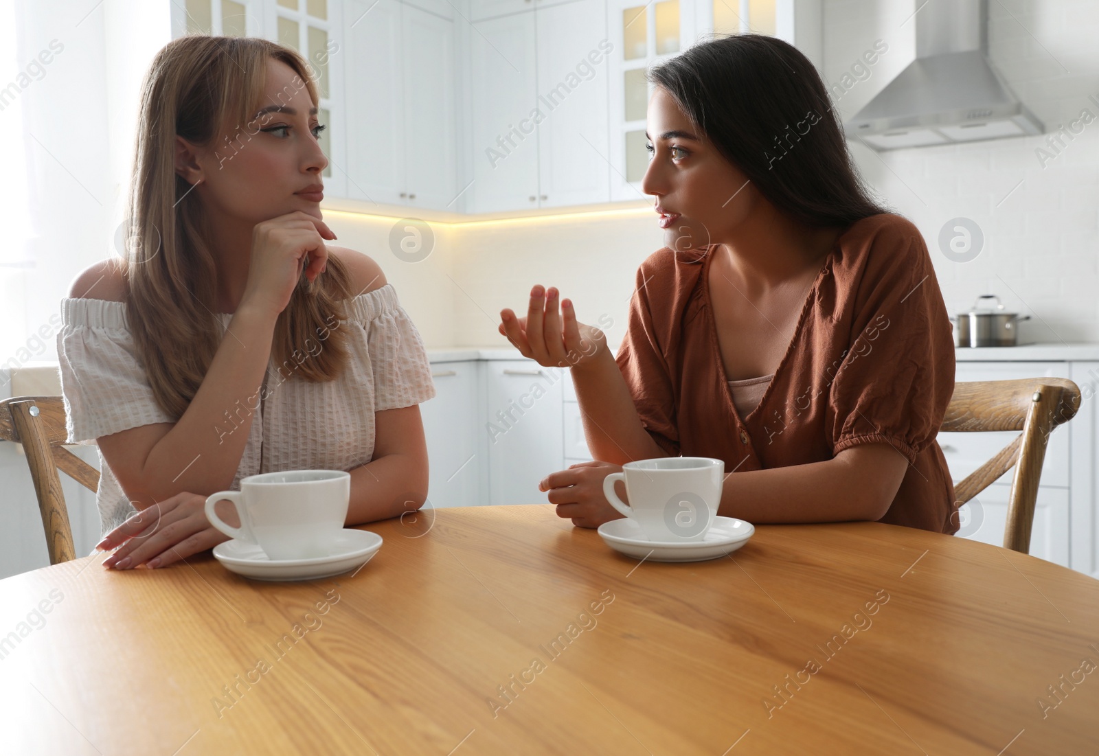 Photo of Young women talking while drinking tea at table in kitchen