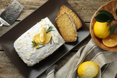 Photo of Tasty lemon cake with glaze and citrus fruits on wooden table, flat lay
