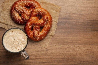 Tasty pretzels and glass of beer on wooden table, flat lay. Space for text
