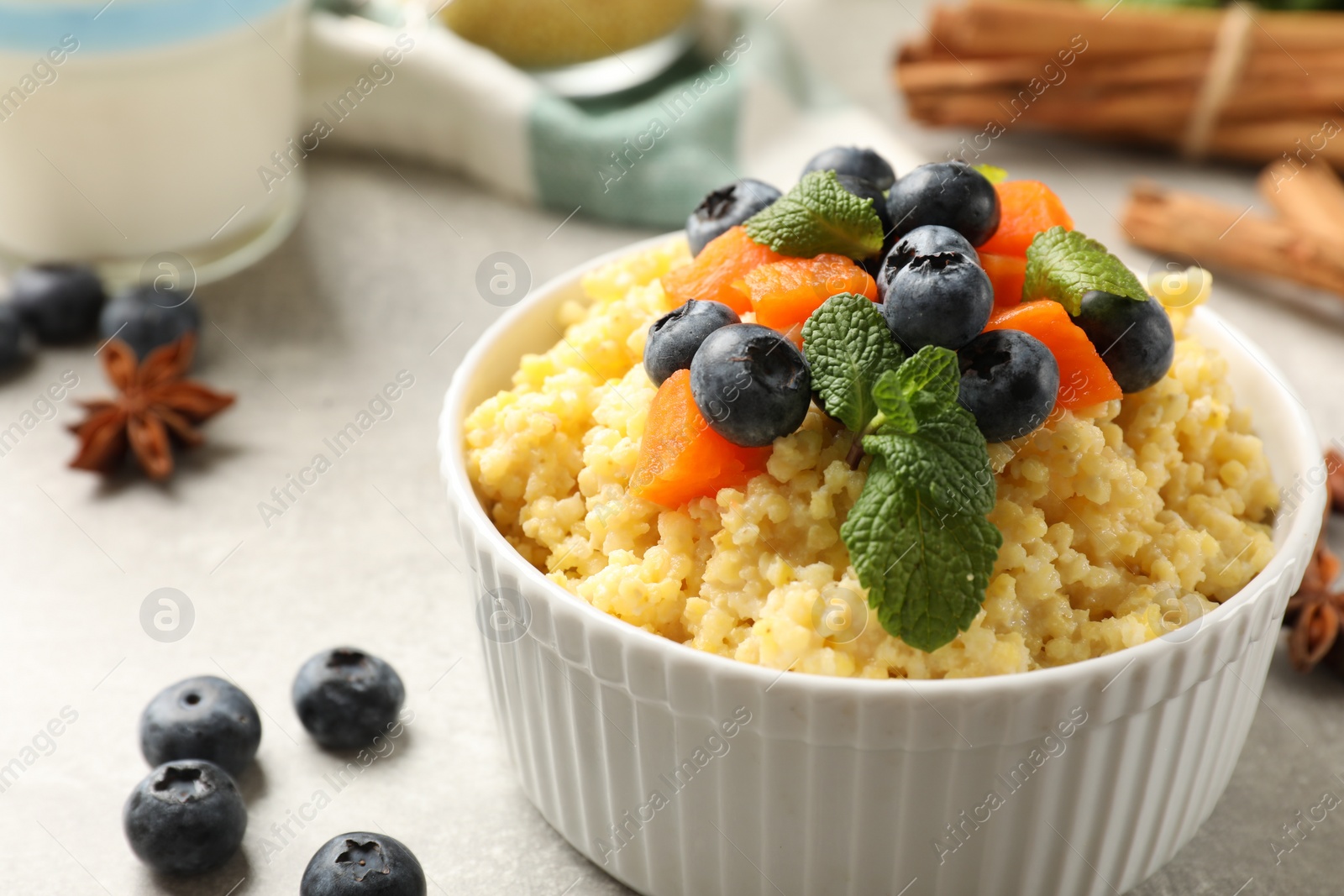 Photo of Tasty millet porridge with blueberries, pumpkin and mint in bowl on light grey table, closeup. Space for text