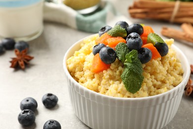 Tasty millet porridge with blueberries, pumpkin and mint in bowl on light grey table, closeup. Space for text