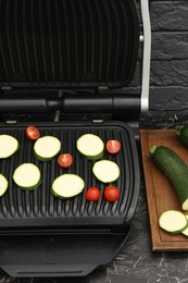 Photo of Electric grill with vegetables on black marble table