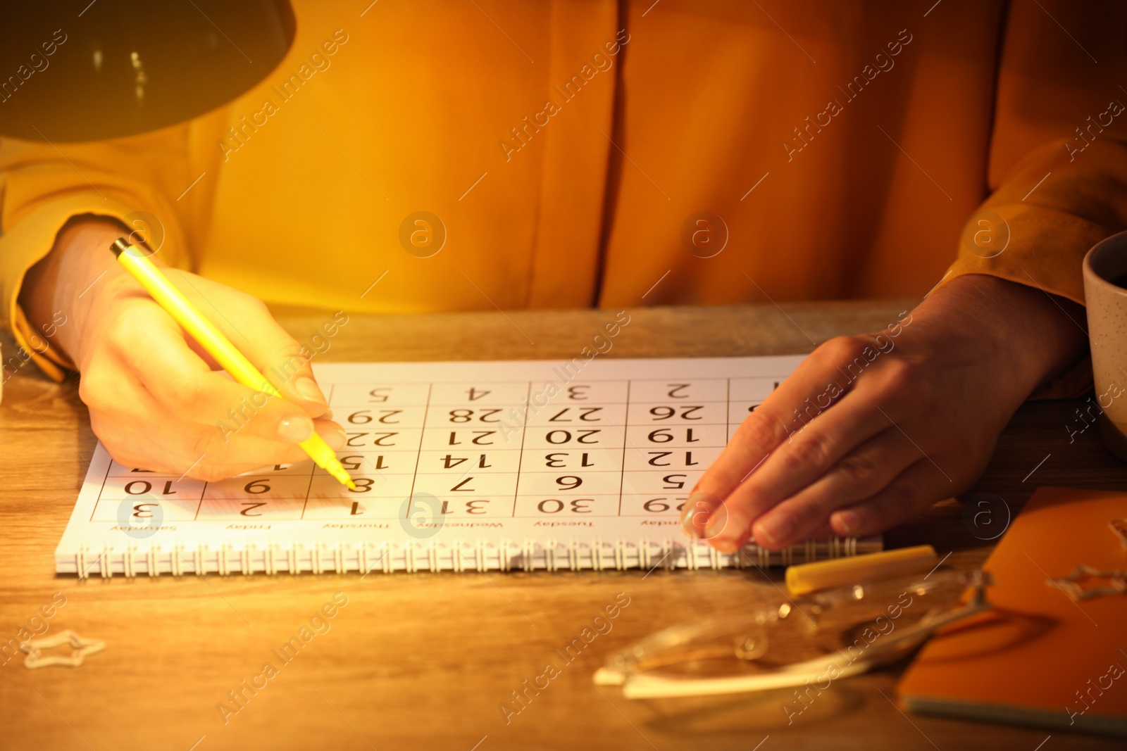 Photo of Woman marking date in calendar at wooden table, closeup