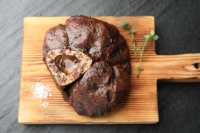 Photo of Piece of delicious grilled beef meat, thyme and salt on black table, top view