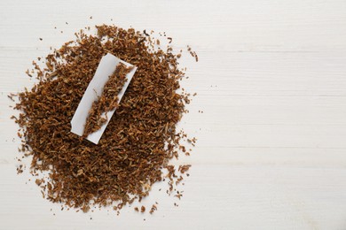 Photo of Heap of tobacco and paper on white wooden table, top view with space for text. Making hand rolled cigarettes