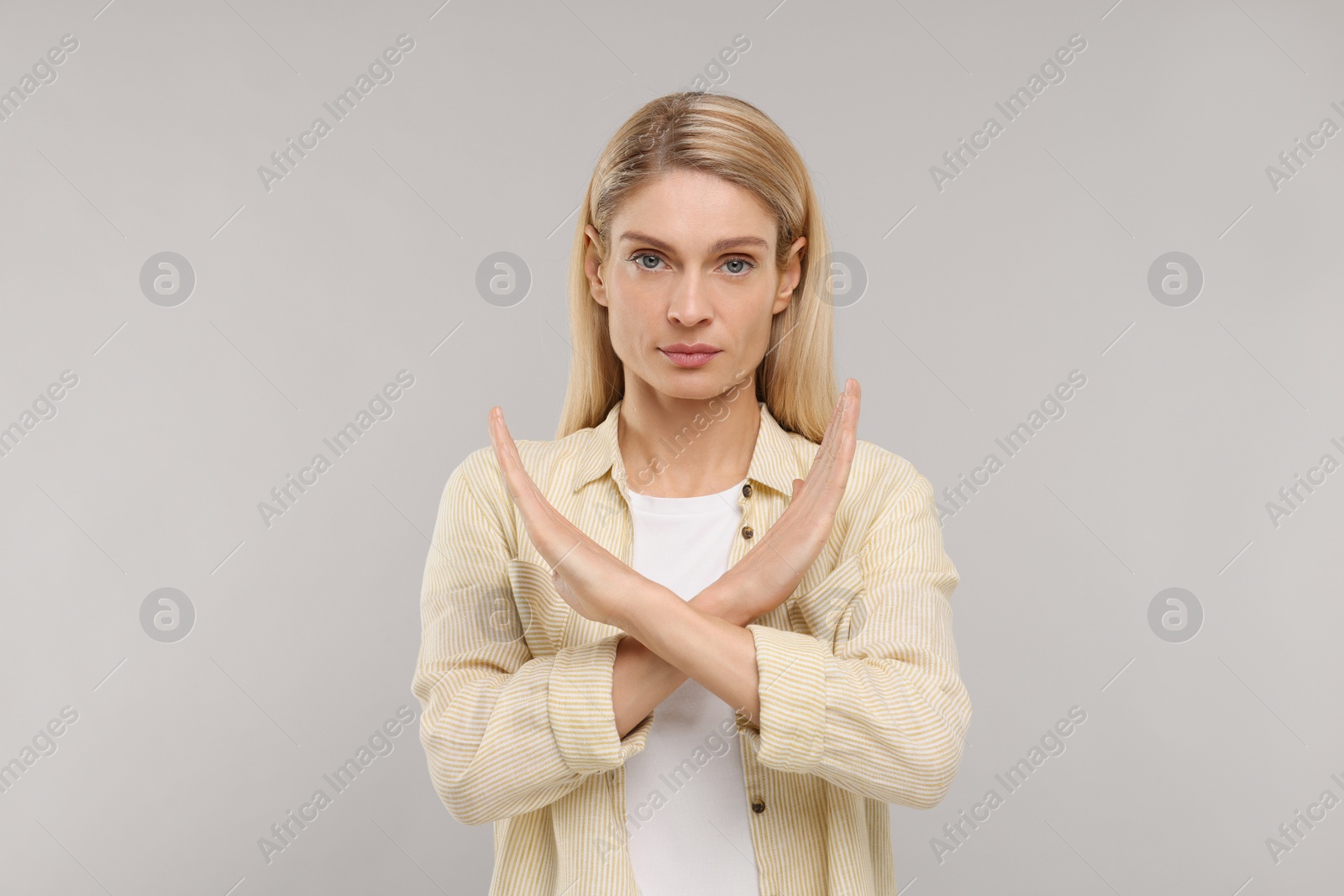 Photo of Stop gesture. Woman with crossed hands on grey background