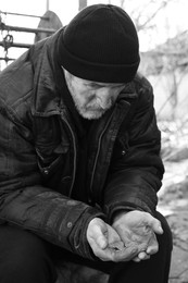 Photo of Poor homeless senior man holding coins outdoors. Black and white effect